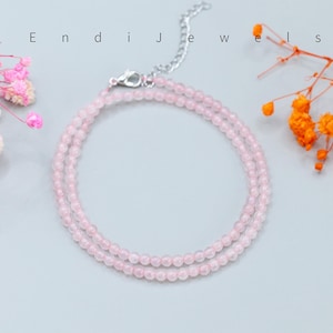 May include: A delicate necklace featuring small, round, pale pink beads arranged in a double-strand design. The piece includes a silver-toned metal lobster clasp and an adjustable chain extension. The text Endi Jewels is visible above the necklace.
