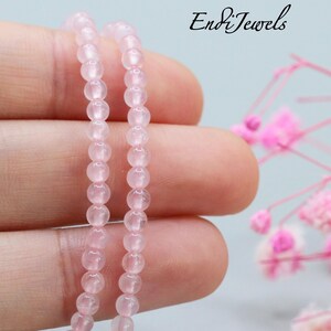 May include: A strand of smooth, round, pale pink rose quartz beads. The text EndiJewels is visible in the upper right corner. The beads are translucent with a polished finish, arranged in a single vertical line against a neutral background.