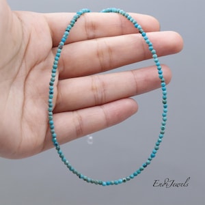 May include: Delicate turquoise bead necklace. The necklace is composed of small, round, light blue beads strung together. The beads are held in a hand against a gray background. The necklace is approximately 16 inches long.