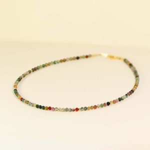 Puede incluir: Un delicado collar hecho de pequeñas cuentas multicolores. Las cuentas son una mezcla de verde, marrón, rojo y rosa.