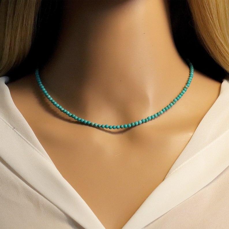 Puede incluir: Un collar de cuentas turquesa puesto en el cuello de una modelo. El collar est&aacute; hecho de peque&ntilde;as cuentas redondas y tiene un dise&ntilde;o simple y delicado.