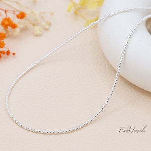 以下が含まれることがあります： 白い背景に置かれた、銀色のビーズのネックレス。ネックレスは小さく丸いビーズでできており、約46cmの長さです。