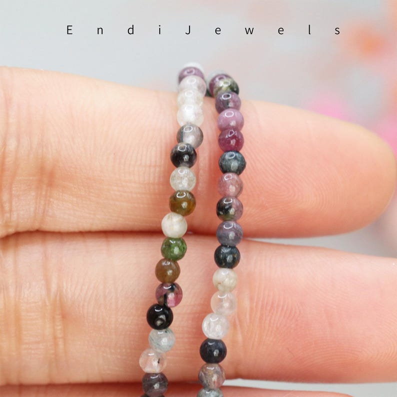May include: Two strands of multi-colored gemstone beads, one strand is clear and the other is pink, green, and black.