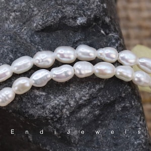 May include: A strand of white oval-shaped pearls. The pearls are strung on a clear thread and are arranged in a loose, flowing pattern.