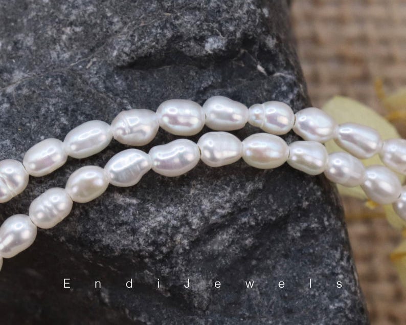 May include: A strand of white oval-shaped pearls. The pearls are strung on a clear thread and are arranged in a loose, flowing pattern.