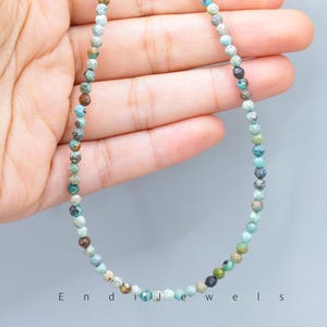May include: A delicate necklace composed of small, faceted beads in shades of turquoise, brown, and gray. The beads are strung together to form a necklace. The word "Endi Jewels" is printed at the bottom of the image.