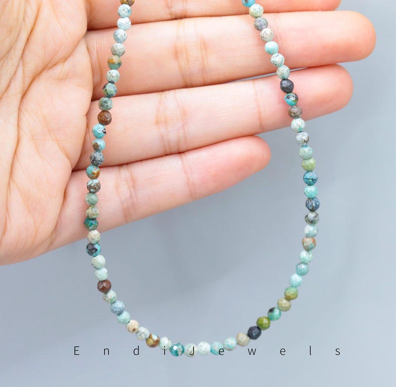 May include: A delicate necklace composed of small, faceted beads in shades of turquoise, brown, and gray. The beads are strung together to form a necklace. The word "Endi Jewels" is printed at the bottom of the image.