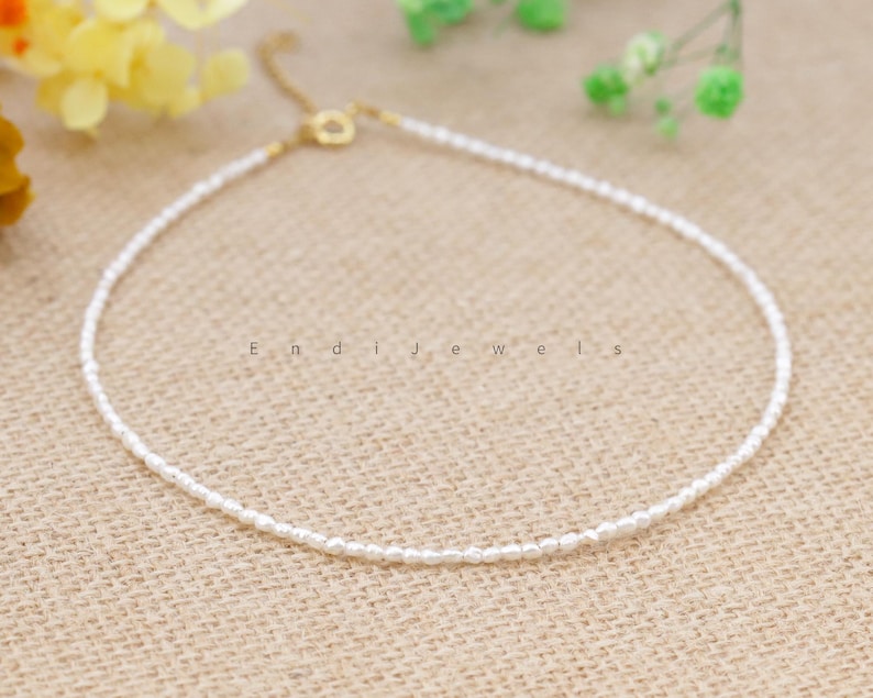 May include: A delicate white pearl necklace with a gold clasp. The necklace is made of small, evenly spaced pearls and is perfect for layering with other necklaces.