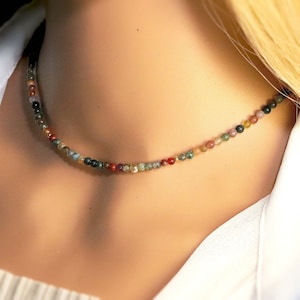 May include: A delicate necklace made of small, multi-colored gemstone beads. The beads are a mix of green, brown, red, and white.