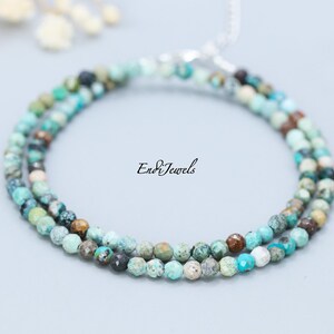 May include: A delicate turquoise beaded necklace with a silver clasp. The necklace is composed of small, round beads in shades of turquoise, brown, and green. The text "EndiJewels" is printed on the right side of the image.