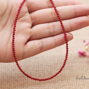 Op de afbeelding: Een delicate rode kralenketting. De ketting bestaat uit kleine, ronde kralen die aan elkaar zijn geregen. De kralen hebben een levendige rode kleur en de ketting wordt gepresenteerd tegen een neutrale achtergrond.