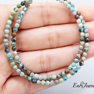 May include: Two strands of turquoise gemstone beads. The beads are small, faceted, and in shades of blue, green, and brown. The beads are strung together, forming a necklace or bracelet. The image includes the text "EndiJewels".