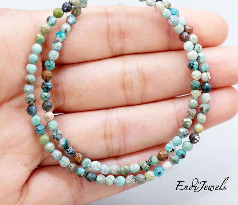 May include: Two strands of turquoise gemstone beads. The beads are small, faceted, and in shades of blue, green, and brown. The beads are strung together, forming a necklace or bracelet. The image includes the text "EndiJewels".