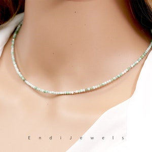 May include: A delicate necklace made of small, light green and white beads. The necklace is on a model's neck and is about 16 inches long.