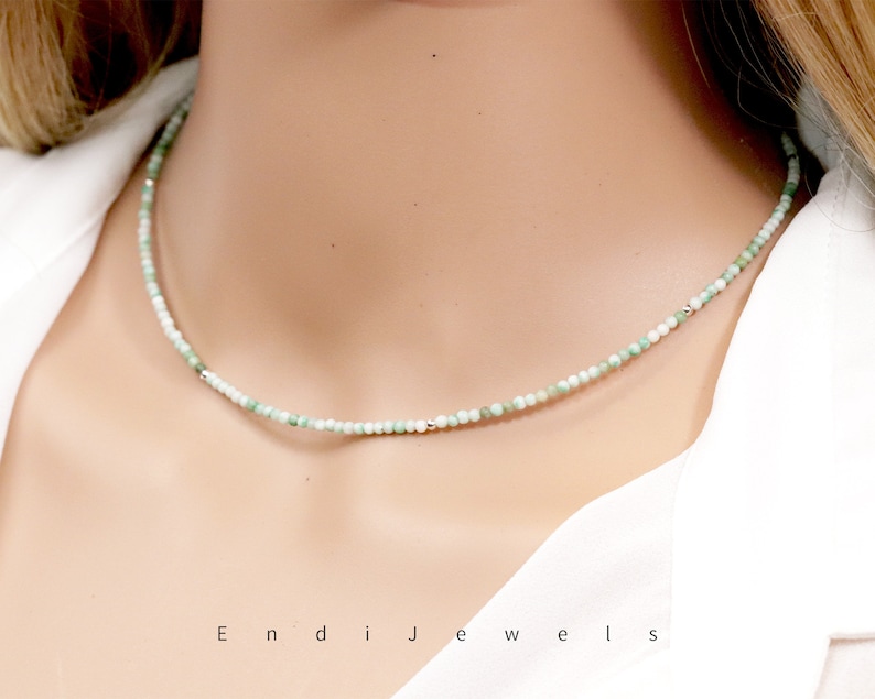 May include: A delicate necklace made of small, light green and white beads. The necklace is on a model's neck and is about 16 inches long.
