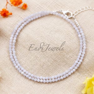 May include: A delicate, light blue beaded bracelet with a silver clasp. The bracelet is made of small, round beads and is displayed on a neutral-toned surface. The text "Endi Jewels" is visible on the surface.