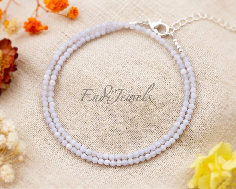 May include: A delicate, light blue beaded bracelet with a silver clasp. The bracelet is made of small, round beads and is displayed on a neutral-toned surface. The text "Endi Jewels" is visible on the surface.
