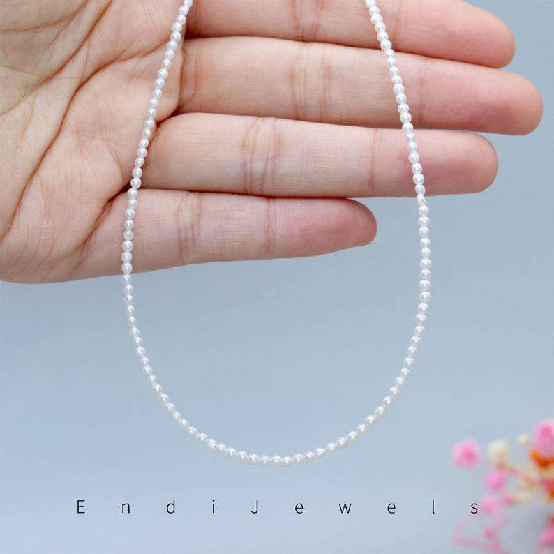 May include: Delicate white pearl necklace. The necklace is composed of numerous small, round pearls strung together. The pearls are a bright white color and create a simple, elegant design. The necklace is displayed against a light blue background.