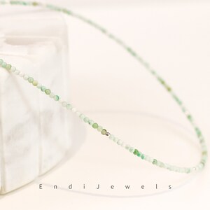 May include: A delicate green gemstone necklace with silver beads. The necklace is made of small, round beads and is strung on a silver chain.
