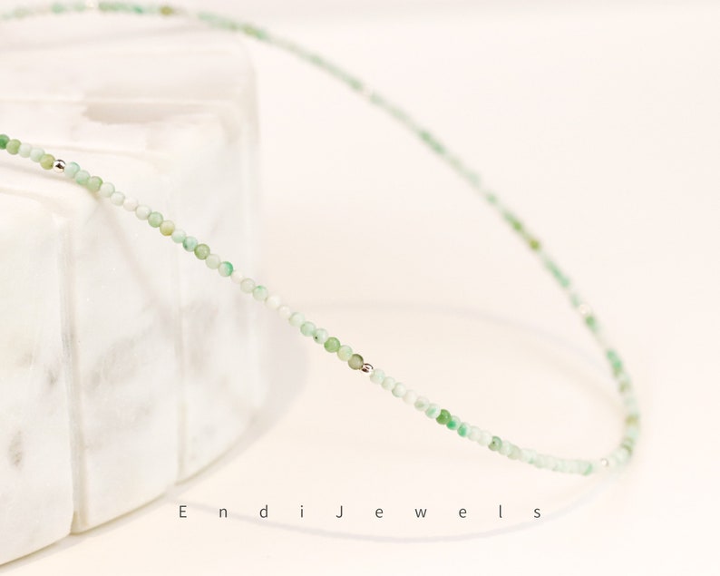 May include: A delicate green gemstone necklace with silver beads. The necklace is made of small, round beads and is strung on a silver chain.