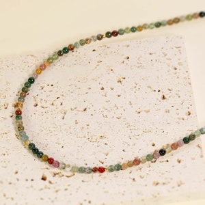 May include: A multi-colored agate bead necklace with gold accents. The necklace is made of small, round beads in shades of green, brown, red, and pink.