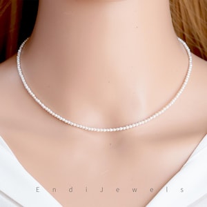 May include: Delicate white pearl necklace. The necklace is composed of small, round pearls strung together, creating a simple yet elegant design. The necklace is worn around the neck, showcasing its delicate nature. The brand name "Endi Jewels" is visible at the bottom.