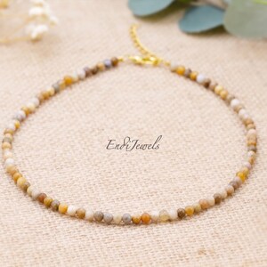 May include: A delicate beaded bracelet featuring small, round, multi-colored beads in shades of beige, brown, and yellow. The bracelet has a gold-colored clasp and chain. The text "Endi Jewels" is visible.