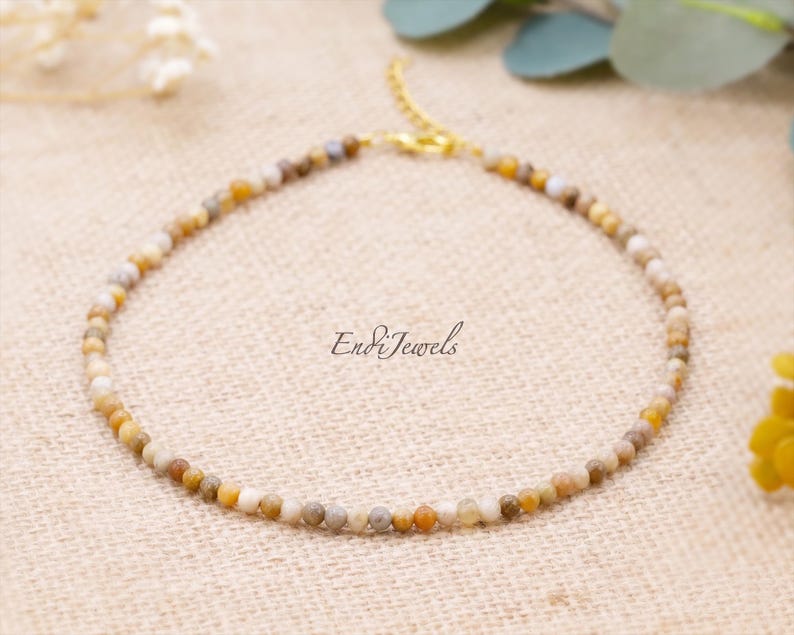 May include: A delicate beaded bracelet featuring small, round, multi-colored beads in shades of beige, brown, and yellow. The bracelet has a gold-colored clasp and chain. The text "Endi Jewels" is visible.