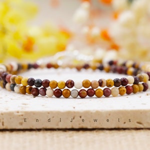May include: A double-strand bracelet made with small, colorful gemstone beads. The beads are in shades of red, orange, yellow, brown, and white. The bracelet is on a white surface with the text "Endi Jewels" printed on it.