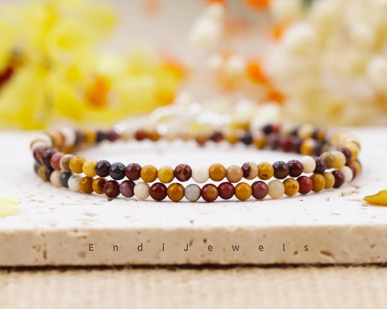 May include: A double-strand bracelet made with small, colorful gemstone beads. The beads are in shades of red, orange, yellow, brown, and white. The bracelet is on a white surface with the text "Endi Jewels" printed on it.