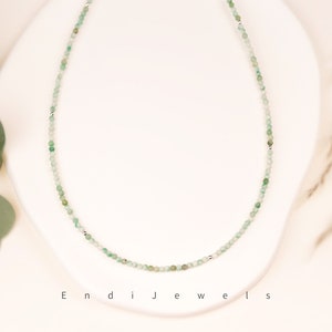 May include: A delicate silver chain necklace with small green gemstone beads. The necklace is on a white background.