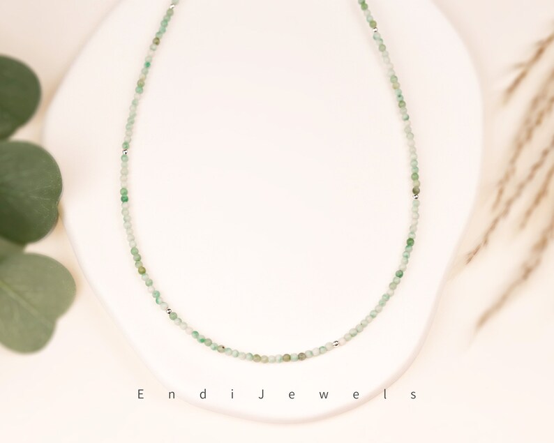 May include: A delicate silver chain necklace with small green gemstone beads. The necklace is on a white background.