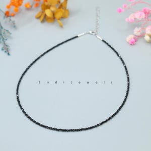 May include: A delicate black gemstone necklace with a silver clasp. The necklace is made of small, round black gemstones that are strung together on a silver chain.