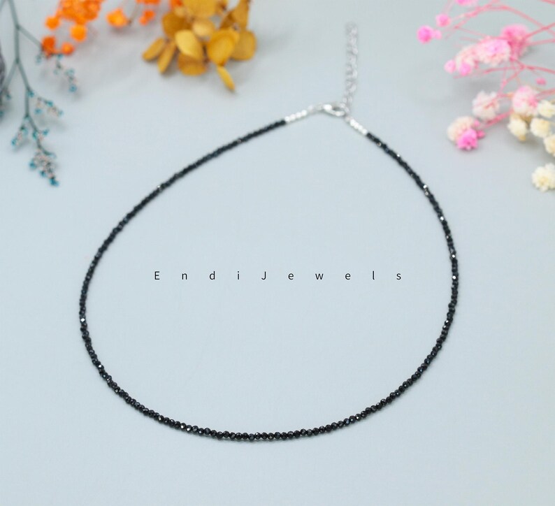 May include: A delicate black gemstone necklace with a silver clasp. The necklace is made of small, round black gemstones that are strung together on a silver chain.