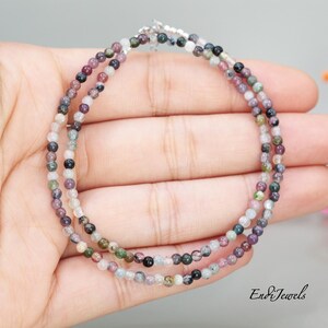 May include: A multi-colored gemstone beaded bracelet with a silver clasp. The beads are small and round, and they are arranged in a random pattern. The bracelet is on a hand, but the hand is not visible in the image.