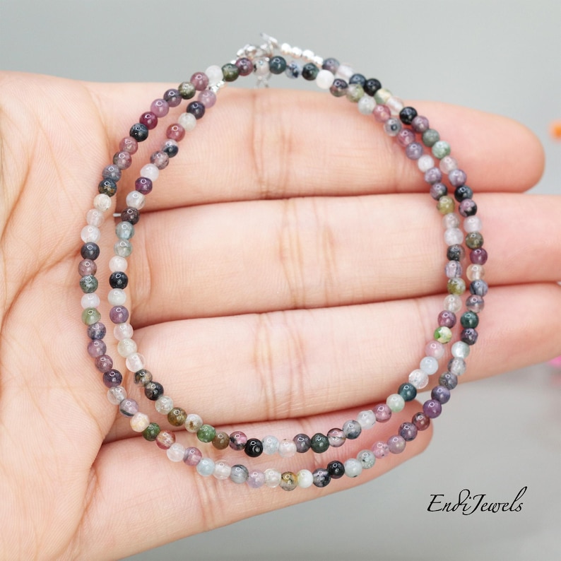 May include: A multi-colored gemstone beaded bracelet with a silver clasp. The beads are small and round, and they are arranged in a random pattern. The bracelet is on a hand, but the hand is not visible in the image.
