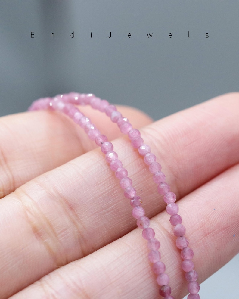May include: Close-up of a delicate pink gemstone bead necklace. The beads are small and faceted, strung together to create a subtle sparkle. The necklace is held in a hand, with the brand name "Endi Jewels" visible at the top.