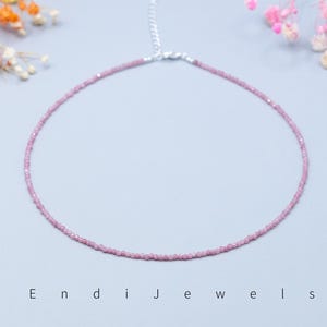 May include: A delicate pink gemstone necklace with a silver clasp. The necklace is composed of small, evenly sized beads, creating a continuous, circular design. The background is a soft, light blue, with floral accents in the corners. The text "Endi Jewels" is at the bottom.