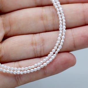 May include: Two delicate strands of white pearl necklace. The pearls are small and evenly sized, creating a refined and elegant look. The necklace is shown against a neutral background, highlighting the jewelry's simplicity and beauty. The text "Endi Jewels" is at the bottom.