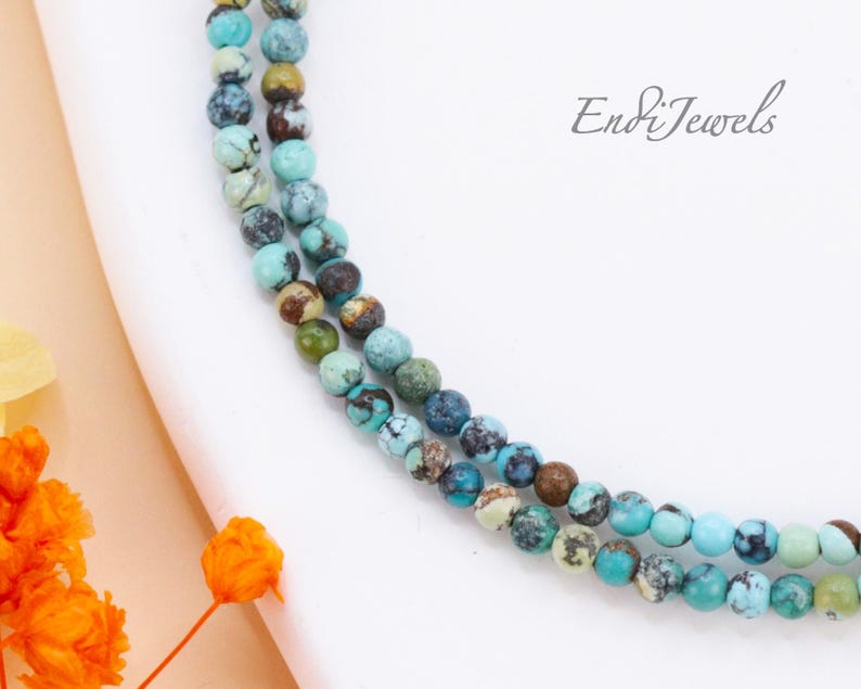 Op de afbeelding: Een dubbele streng turquoise edelsteen kralen in tinten blauw, groen en bruin. De kralen zijn rond en hebben een gevlekt patroon. De kralen zijn geregen op een doorzichtig koord.