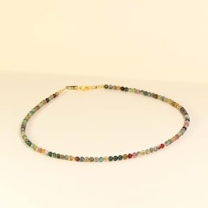 May include: A delicate necklace made of small, multi-colored gemstone beads. The beads are a mix of green, brown, pink, and yellow.