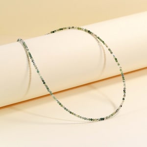 Puede incluir: Un delicado collar de cuentas verdes y plateadas. El collar está hecho de pequeñas cuentas redondas que están enhebradas en una fina cadena plateada.