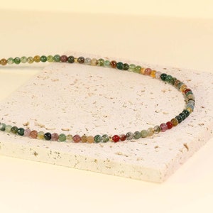 May include: A multi-colored beaded necklace with green, brown, red, and pink beads. The necklace is made of natural stone and is strung on a gold chain.