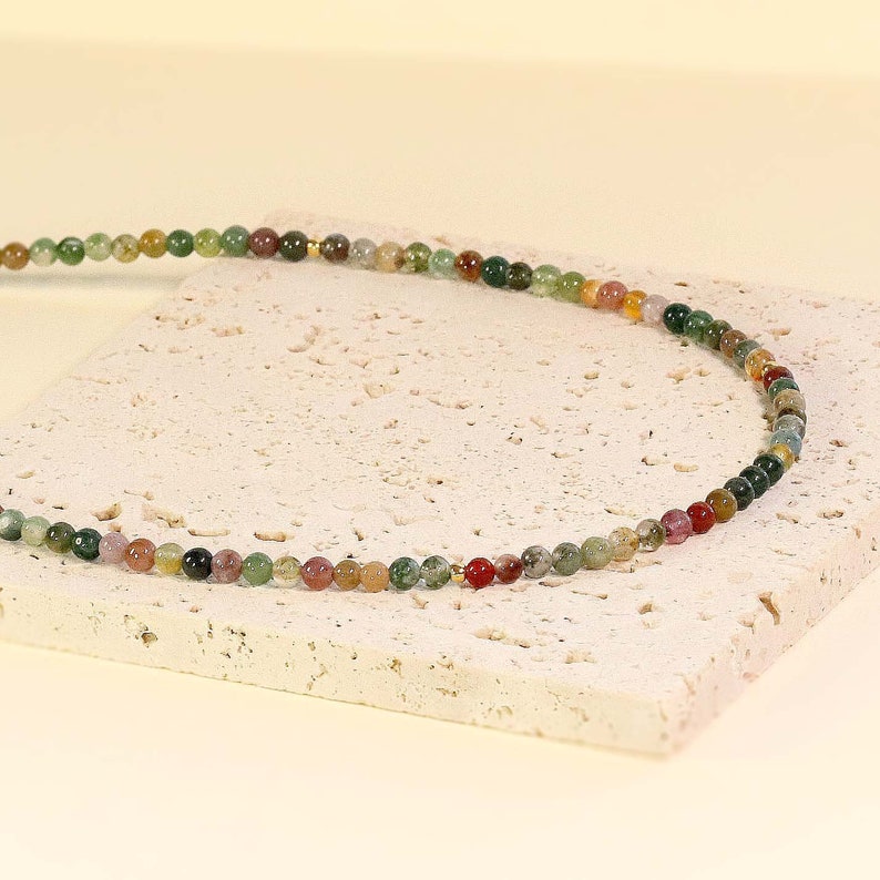May include: A multi-colored beaded necklace with green, brown, red, and pink beads. The necklace is made of natural stone and is strung on a gold chain.