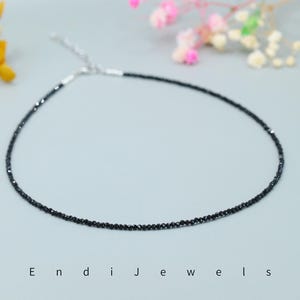 May include: A delicate black diamond necklace with a silver clasp. The necklace is made of small, round black diamonds that are strung together on a thin silver chain.
