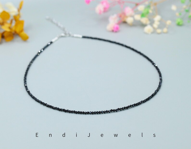 May include: A delicate black diamond necklace with a silver clasp. The necklace is made of small, round black diamonds that are strung together on a thin silver chain.