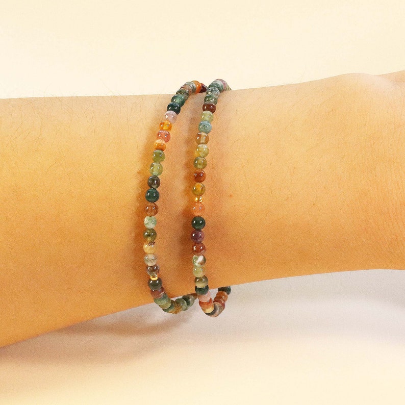 May include: A multi-colored beaded bracelet with green, brown, orange, and red beads. The bracelet is made of small, round beads and is worn on a person's wrist.