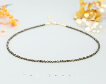 May include: A delicate gold chain necklace with small, dark grey gemstone beads. The necklace is on a white background.