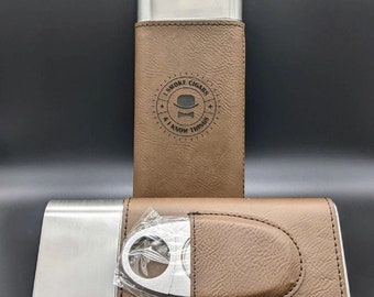 Puede incluir: Un estuche para cigarros de cuero marrón con interior de acero inoxidable. El estuche tiene un cortador de cigarros incorporado y un diseño grabado que dice "I smoke cigars & I know things".