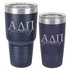 May include: Two stainless steel tumblers with a navy blue finish. The tumblers feature a white design with the letters "ΑΔΠ" and the words "alpha delta pi".